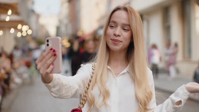 Young woman blogger taking selfie on smartphone video call online with subscribers in city street