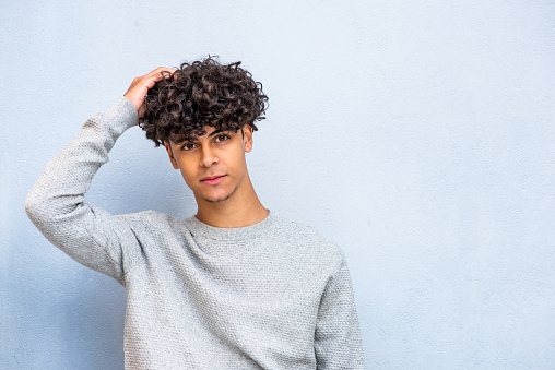 Portrait handsome young North African man posing with hand in hair by blue background