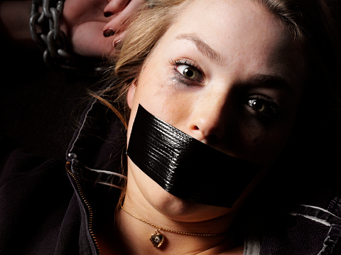 Horror on a female's face being held hostage, tied and bound in chains.