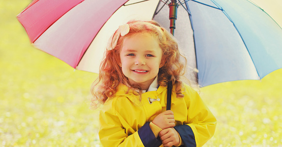 Happy little girl child with colorful umbrella in sunny autumn park