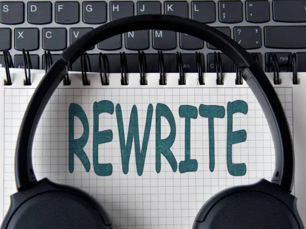 Photo of REWRITE -word on white notepad with keyboard and headphone background