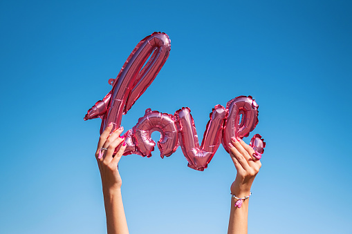 Female hands holding Love word balloon against blue sky.