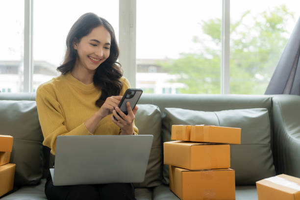 istock A young Asian small business entrepreneur starts using a smartphone and laptop computer to check orders from the web, owns a work at home online seller prepares product parcel packs for delivery. 1606593501
