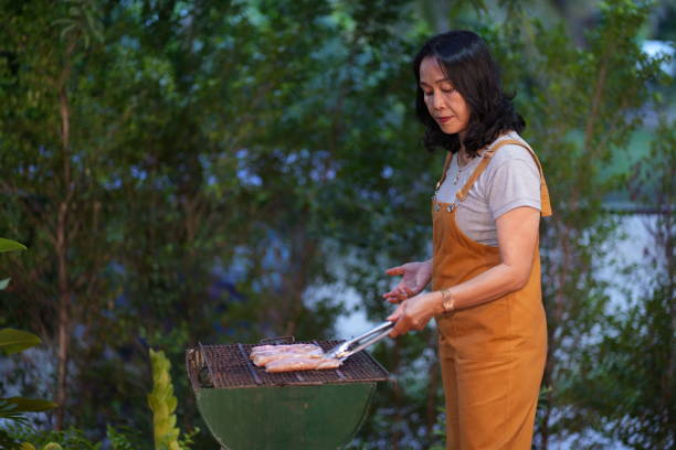 istock Asian woman cooking dinner on barbecue grill at backyard 1606605491