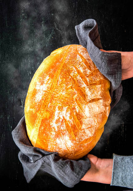istock Female hands hold freshly baked bread on a black background. top view 1606642648