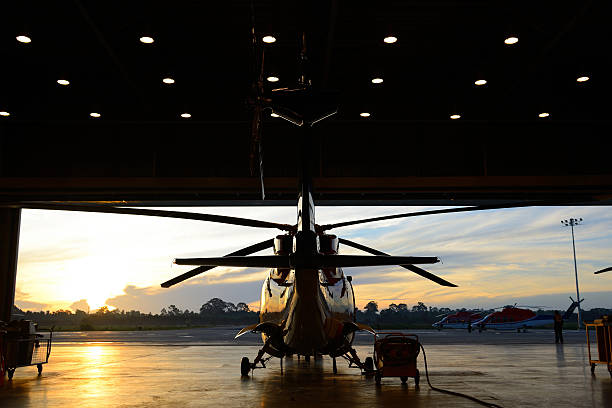 silhouette of helicopter in the hangar silhouette of helicopter in the hangar with sunrise background. airplane hangar stock pictures, royalty-free photos & images