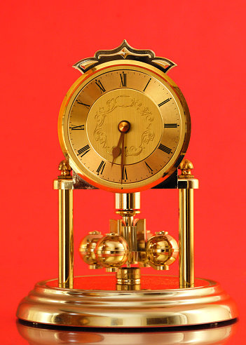 Carriage clock on a ragainst a red background. Slight motion blur on pendulum.