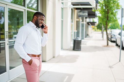 Well-dressed black businessman makes a serious, important phone call while pacing on the sidewalk of a city street.