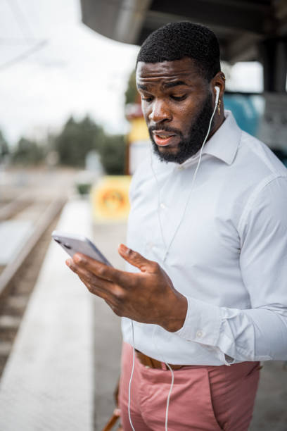 istock Man with earbuds looks at his phone while waiting for train 1606719732