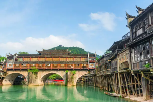 The Hong Bridge (Rainbow Bridge) over the Tuojiang River (Tuo Jiang River) and old authentic traditional Chinese wooden riverside houses on stilts in Phoenix Ancient Town (Fenghuang County), China.