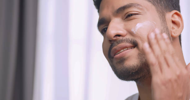 istock Handsome young man applying cream at his face while standing in front of mirror in bathroom at home. 1606756923