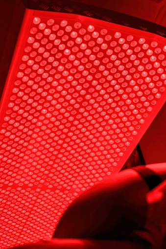 A person lays under a red light therapy bed.