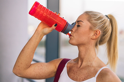 Profile view of a blonde woman in a gym drinking water