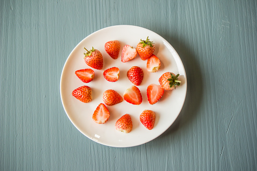Strawberries cut in half and put several pieces on a plate on the ground.