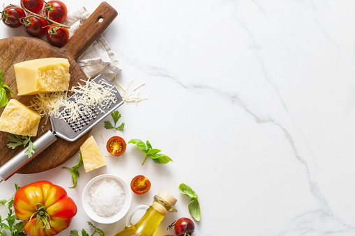 Cooking background with ingredients for preparation healthy food parmesan cheese, basil leaves, cherry tomato, garlic and olive oil on marble table top view