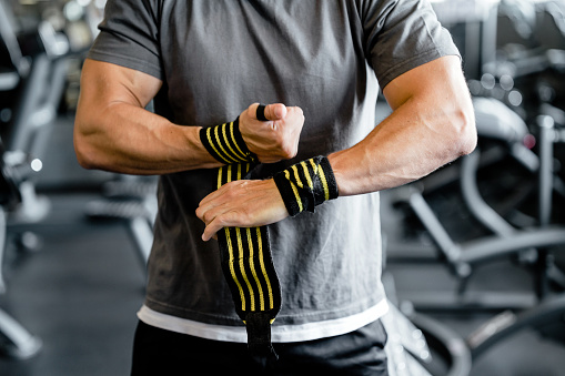 Close-up of fit muscular man putting on straps in gym