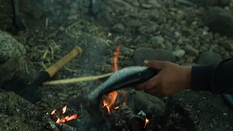 A man puts a fish on a skewer and puts it on a fire