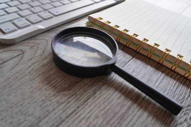 istock Close up image of magnifying glass, notebook and computer keyboard on table. 1607023702