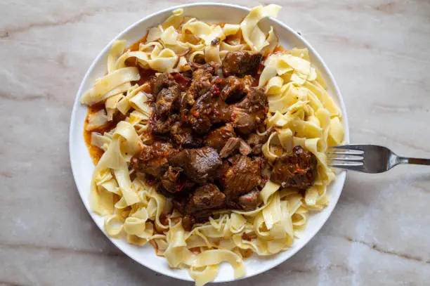 Delicious pork stew or pork ragout with pasta on a plate with fork isolated on light marble background from above with copy space