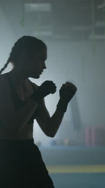 Woman fighter trains his punches and defense in the boxing gym, the girl strikes fast, vertical video.