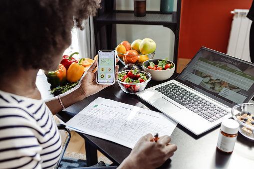 Rear view of an unrecognizable nutritionist using a diet tracker mobile app on her smart phone to create a nutrition plan for the clients