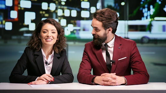 Media team hosting night talk show, discussing about international daily events in news studio. Two journalists addressing all breaking news topics live on television network.