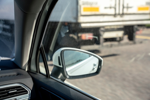 Side-view mirror of the car, defocused semi-truck at the adjacent lane on the background