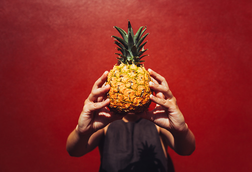 A woman plays with a pineapple in front of a red wall background