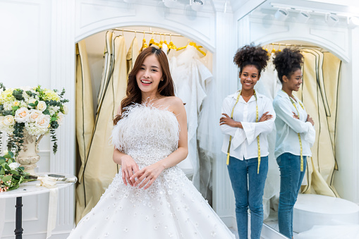 Portrait of beautiful bride and wedding planner look at camera in studio. Attractive bridal shop owner designer women help and support customer choose wedding gown at store. Marriage ceremony concept.