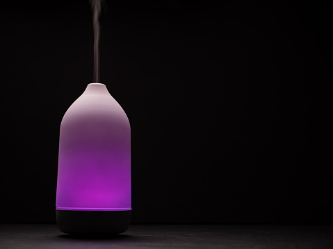 Purple light diffuser diffusing steam on black background. Closeup
