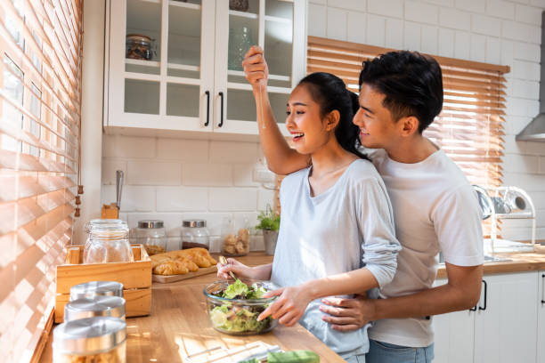 istock Asian romantic man making surprise girlfriend with necklace in kitchen. Attractive romantic new marriage couple male and female spend time celebrate anniversary and valentine's day together in house. 1607108340
