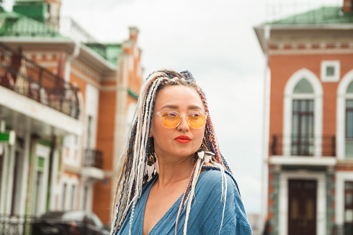 Portrait of a young serious woman with long colored dreadlocks and a nose piercing on a city street on a sunny summer day.