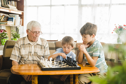 Grandpa and his grandchildren are playing chess sitting on the sofa in the living room
