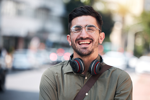 Travel, city and a man outdoor for work on a road with a smile, glasses and headphones. Face portrait of a happy male student on urban street with freedom and pride for casual business internship