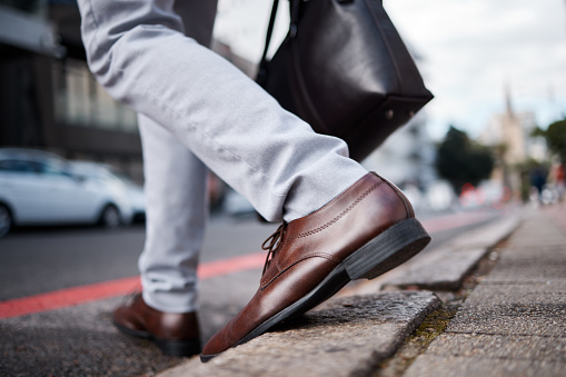 Feet, business man and walking on city road or ground for travel, journey and commute to work. Shoes, legs and closeup of a professional person or employee crossing an urban street with a bag