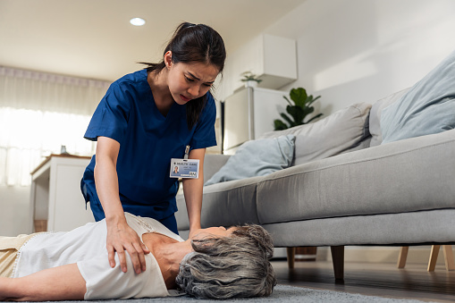 Asian caregiver saving senior woman's life by doing cpr in emergency. Attractive young female carer doctor doing first aid heart massage to unconscious patient with heart attack in living room at home