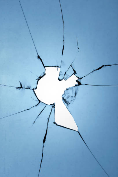 istock Glass texture of a broken window with a hole and cracks on a blue background. 1607157003
