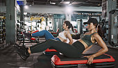 Two young woman doing knee tuck crunches in the gym. Powerful female bodybuilder pumping abs muscles.