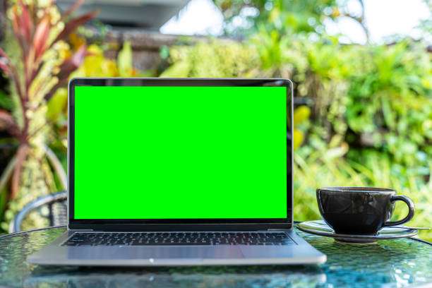 istock Mockup of laptop computer with empty screen with coffee cup and smartphone on table of the coffee shop outdoor background,Green screen 1607198482