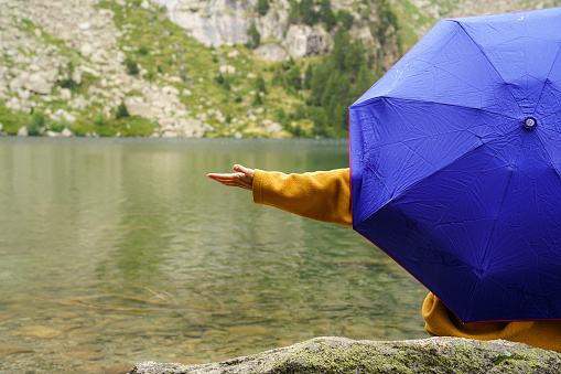 Unrecognizable woman with a blue umbrella raining in the mountains with a lake. bad weather hiking