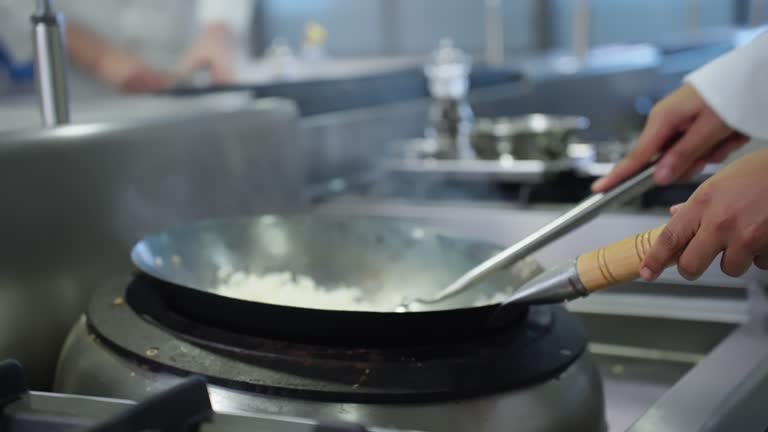 Fried rice cooking preparation in frying pan by ingredients such as cooked rice, fried scrambled egg, fried garlic, and sauces, chefs working in commercial kitchen