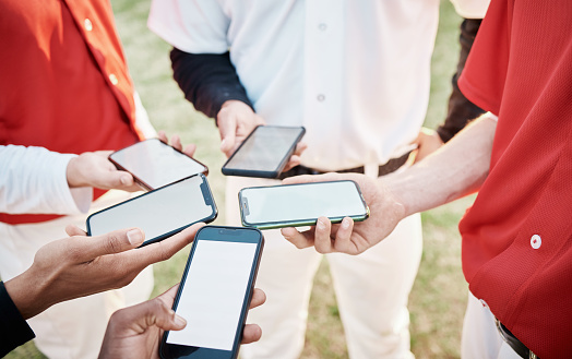 Hands, phone and baseball with a team networking outdoor on a sport field for strategy or tactics before a game. Teamwork, fitness and communication with a group of people sharing sports information