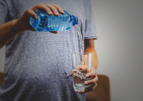 man's hand holding a bottle of water Pouring water into a glass over white background - healthy lifestyle