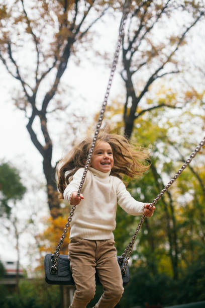 Cheerful little girl swinging on a swing in the public park