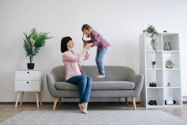 istock Mother helping child jumping on sofa in spacious apartment 1607262212