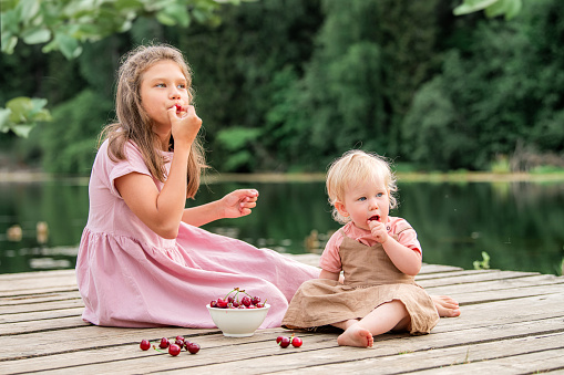 Two little girls sisters eat cherries in nature in the countryside. Healthy food.