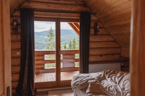 Bedroom with an unmade bed in a wooden chalet overlooking the mountains and the forest. Holidays in the mountains concept