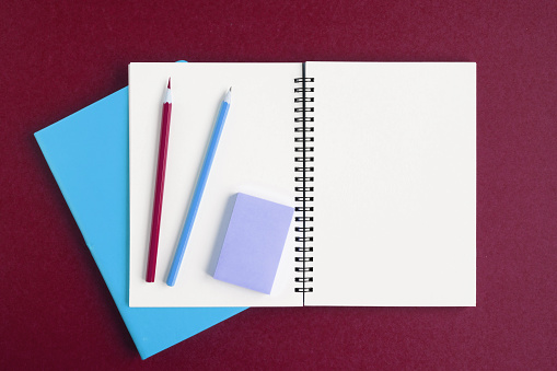 Notebook with pencil. White page on dark red color background, spiral notepad on table. Top view Copy Space. Blank paper sheet, office supplies. Greeting card mockup. Modern Minimal business mock up