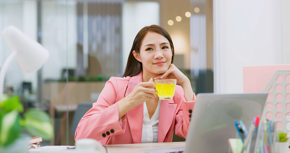 asian business woman is taking vitamin effervescent tablet in glass of water while working with laptop computer at office