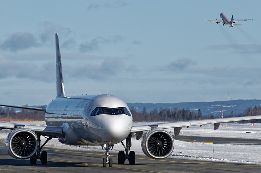 Lufthansa Airbus A320neo taxing at Oslo Airport Gardermoen with plane taking off in the background